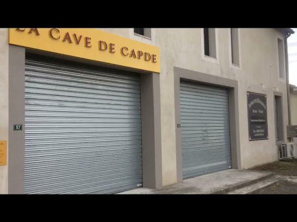 Façade de « La Cave de Capde », avec deux volets métalliques fermés et une enseigne murale