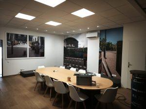Salle de réunion moderne avec grande table ovale, chaises blanches et murs décorés de photos murales urbaines
