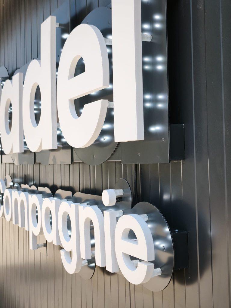 Enseigne lumineuse en lettres blanches sur fond noir, avec le mot « dela compagnie » partiellement visible