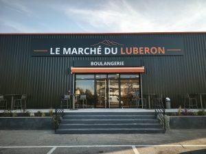 Grand bandeau enseigne Le Marché du Luberon au-dessus de l'entrée de la boulangerie