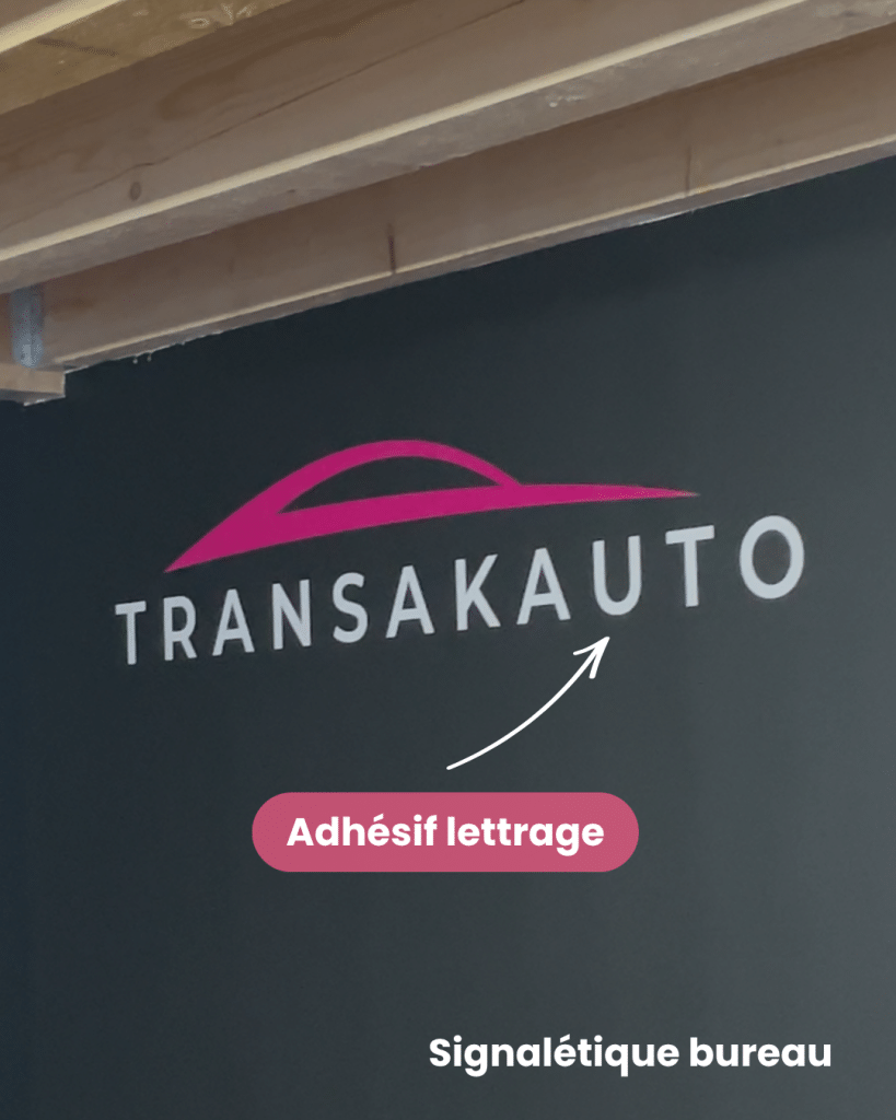 Lettrage adhésif TRANSAKAUTO appliqué sur un mur sombre du bureau — signalétique d'agence