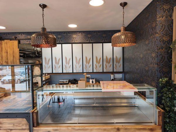 Intérieur de boulangerie avec comptoir en bois, vitrines réfrigérées et suspensions cuivrées
