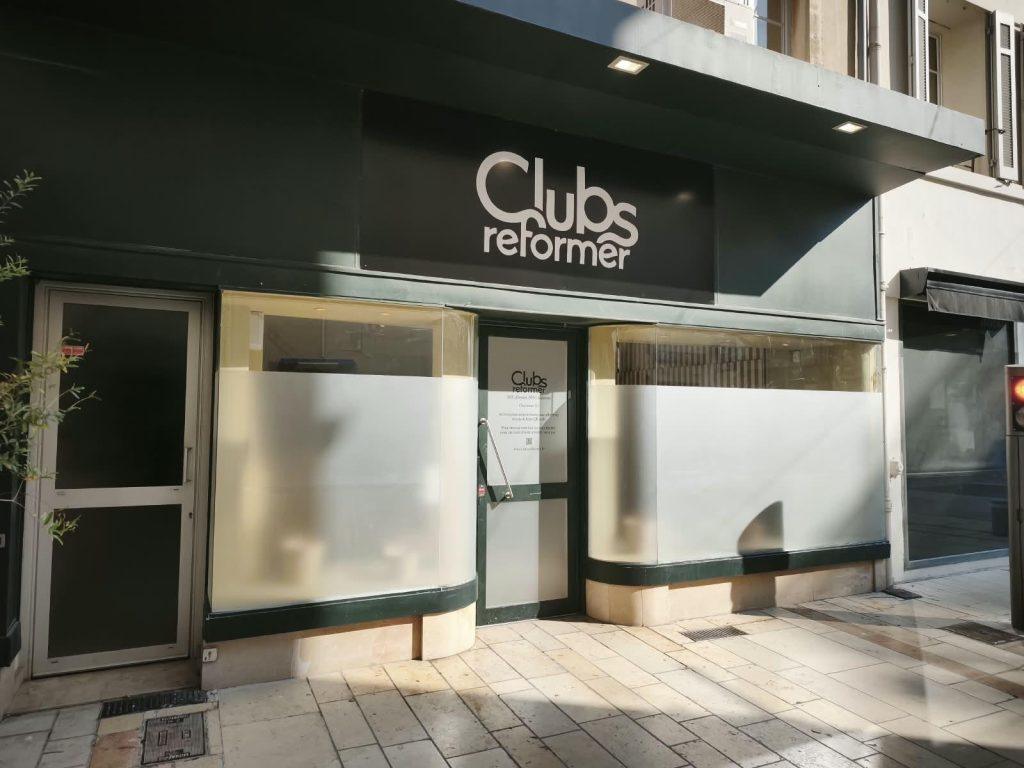 Enseigne 'Clubs reformer' contrastant sur fond noir au-dessus des films opaques