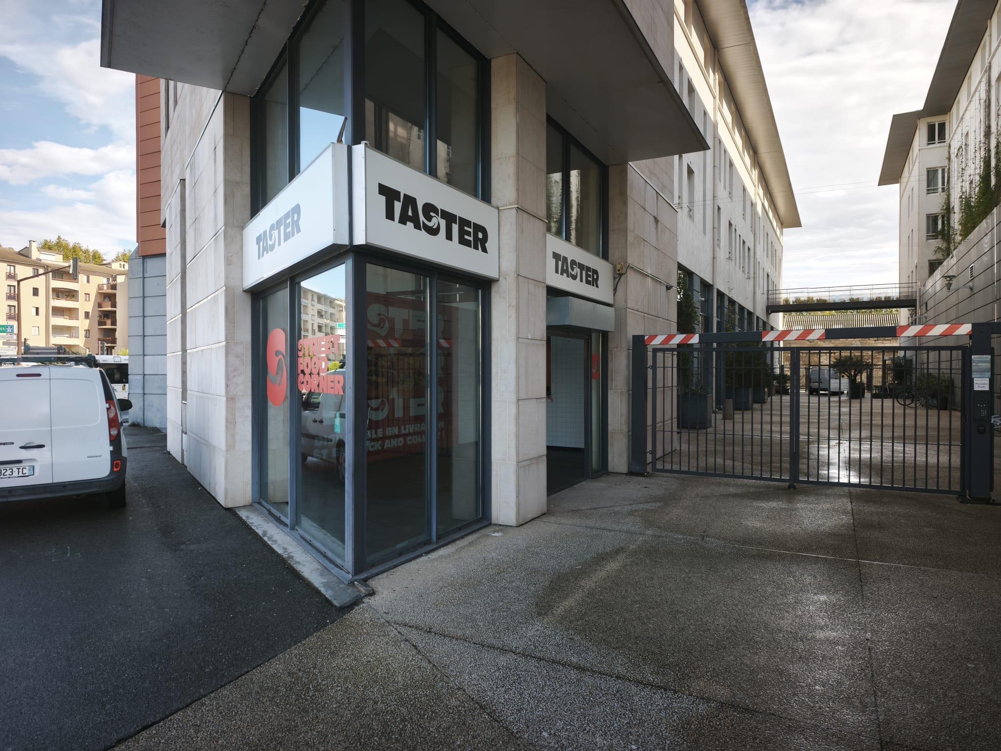 Entrée en angle du magasin Taster avec enseigne blanche et baie vitrée