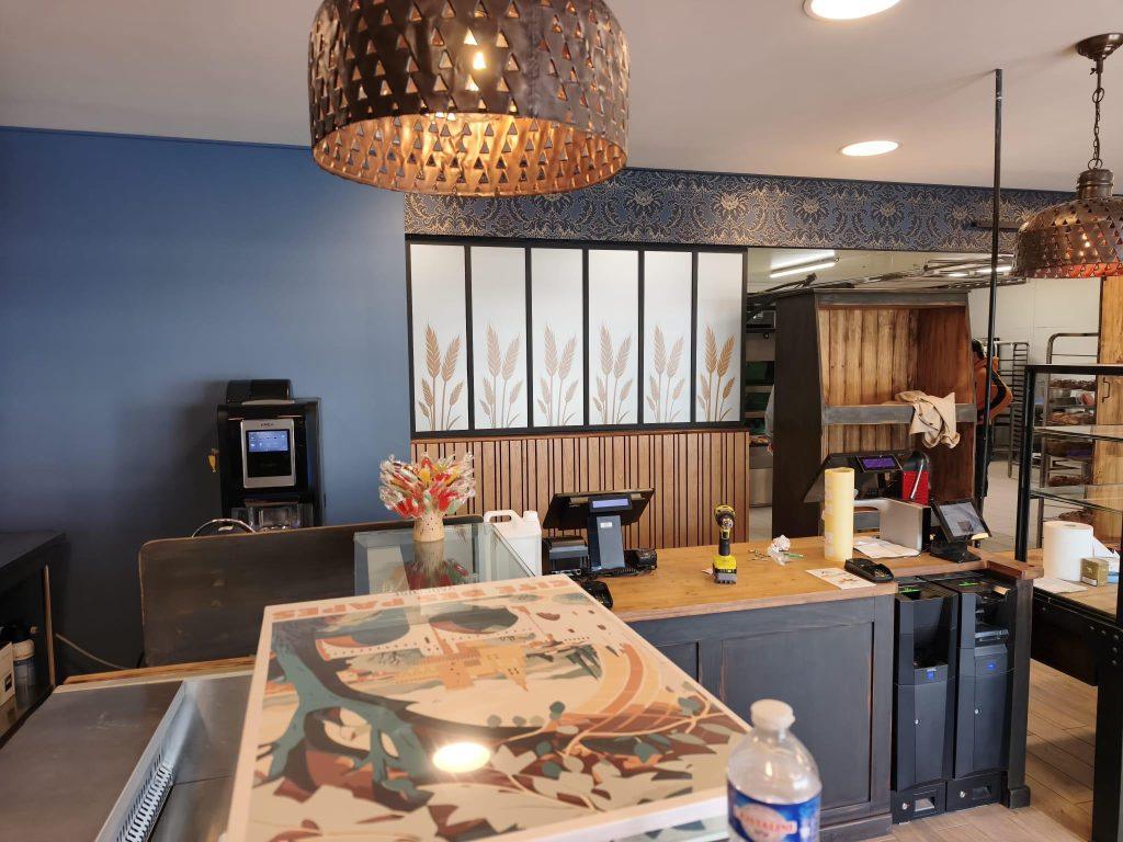 Espace caisse d'une boulangerie avec comptoir illustré, machine à café et suspensions