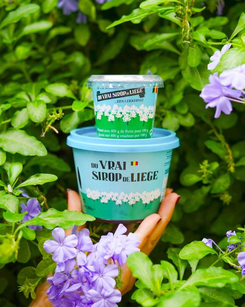 Deux pots turquoise Du Vrai Sirop de Liege posés parmi des fleurs mauves et feuillage