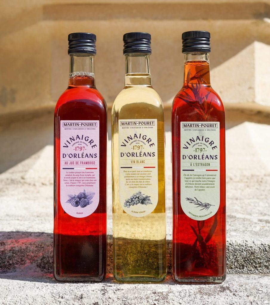 Trois bouteilles Martin‑Pouret Vinaigre d'Orléans alignées sur marches en pierre, couleurs contrastées